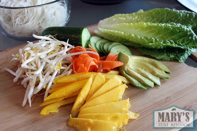 mung bean sprouts, mango, cucumber, lettuce and yellow peppers on a bamboo cutting board.
