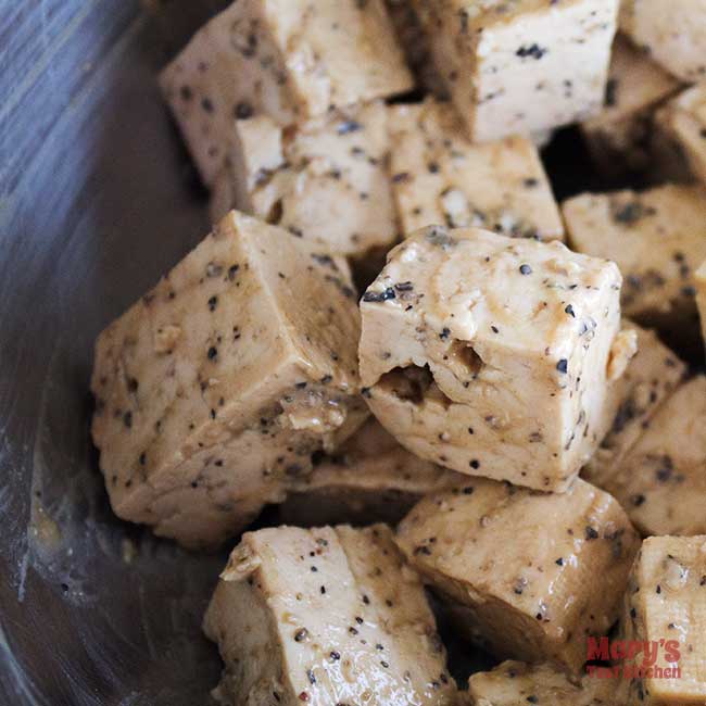 Uncooked bite-sized cubes of tofu coated in black pepper marinade