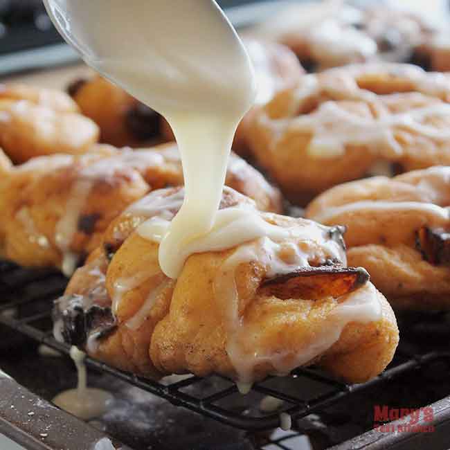 icing being poured on to Vegan Peach Fritters on cooling rack