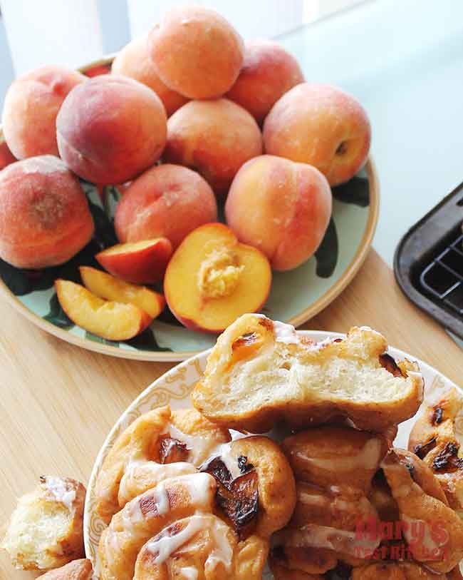 plate of peaches in background with pile of Vegan Peach Fritters in foreground