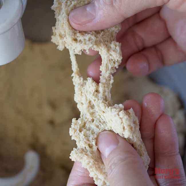 Hands stretching torn piece of seitan dough after first round of kneading