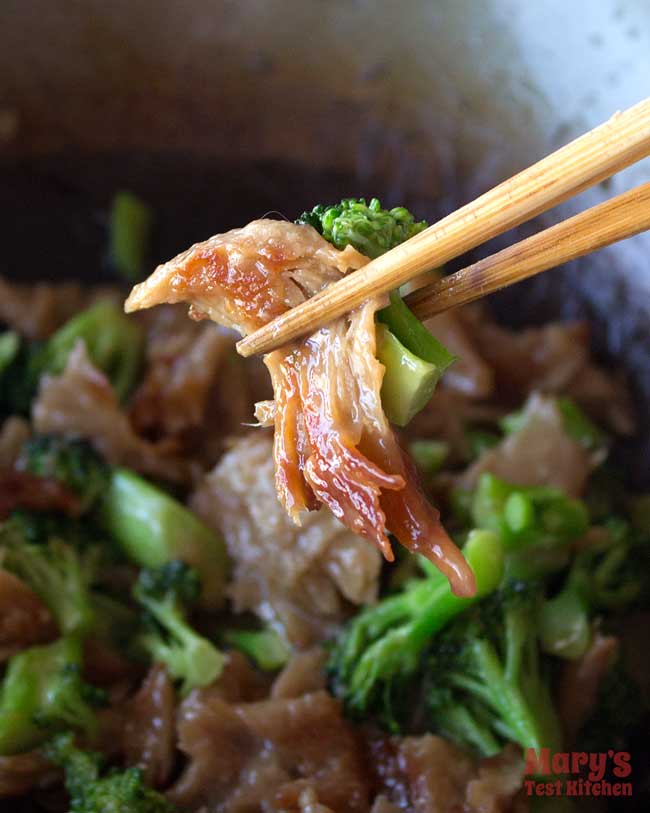 Chopstick holding glossy vegan chicken and broccoli over a wok