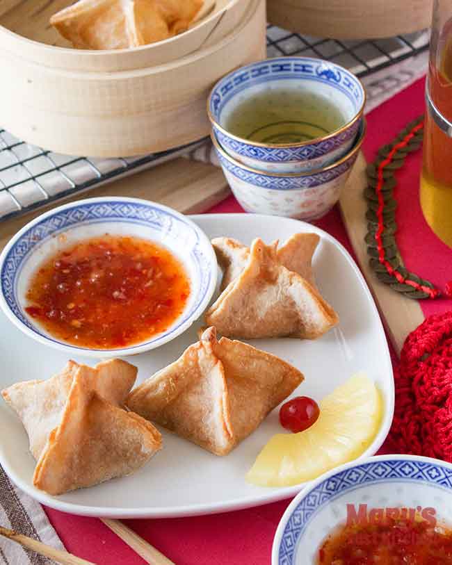 festive plate of vegan crab rangoon with pineapple garnish and sweet chilli sauce