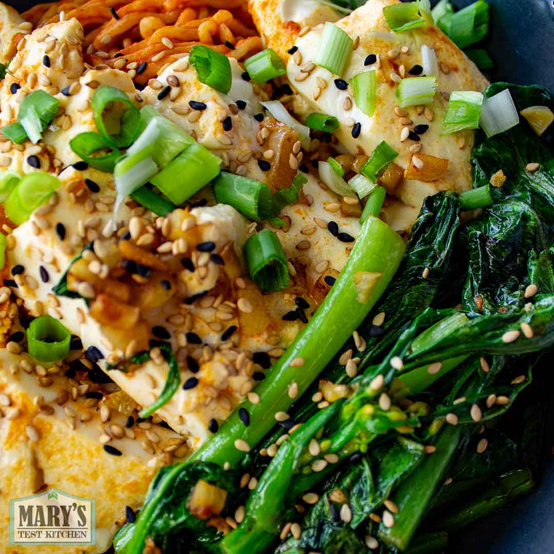 Close up of sauteed choy sum and soft tofu with fire noodles in background