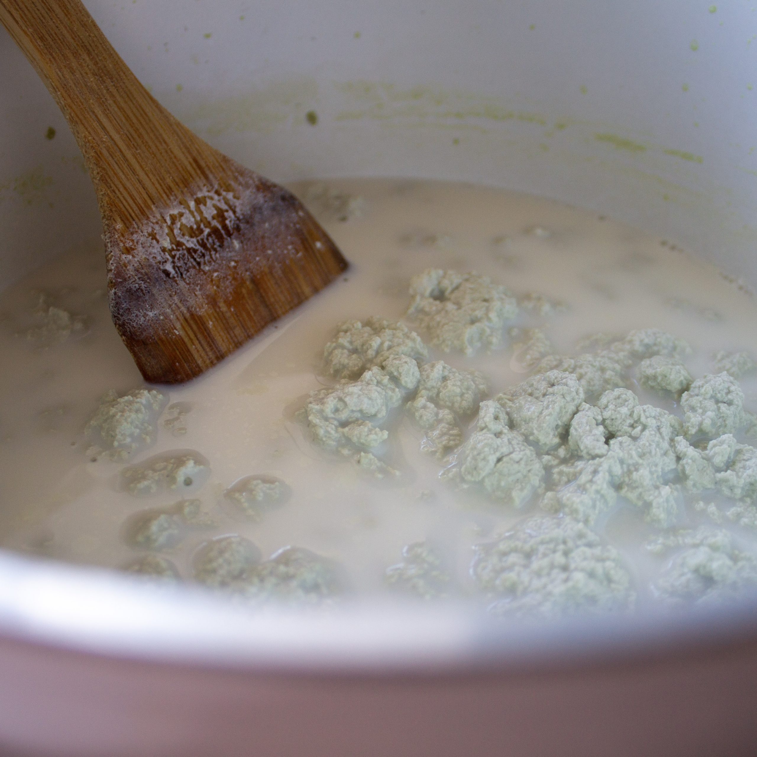 pot of pumpkin seed tofu curds and whey stirred by wooden spatula