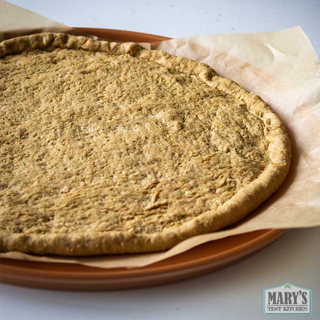 uncooked vegan keto pizza crust in parchment-lined pizza pan