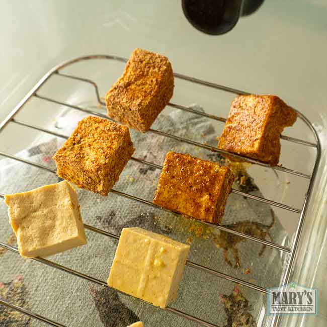 seasoned and unseasoned chickpea tofu cubes in glass basket of airfryer